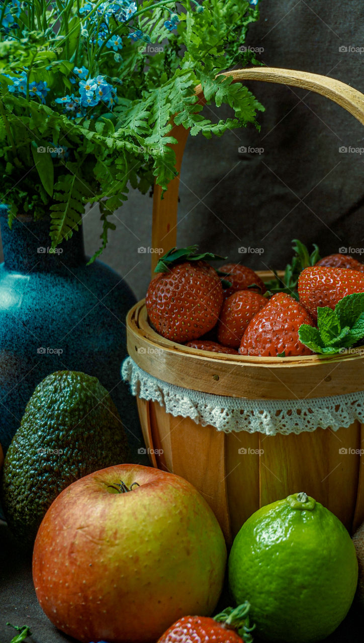 strawberries in a basket with avocado, apples on a dark background