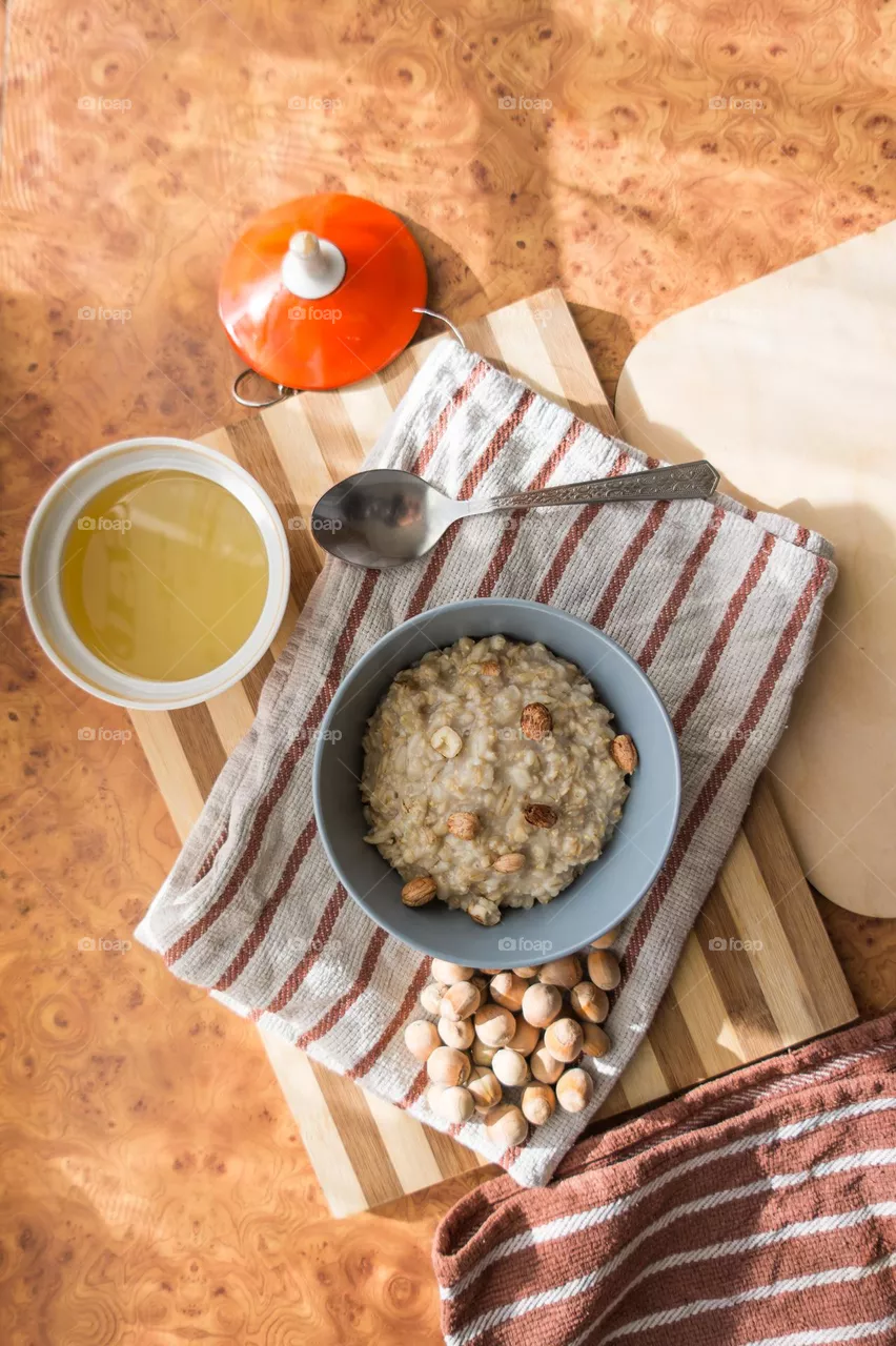 Cooked oatmeal in a deep gray plate with hazelnuts and honey.