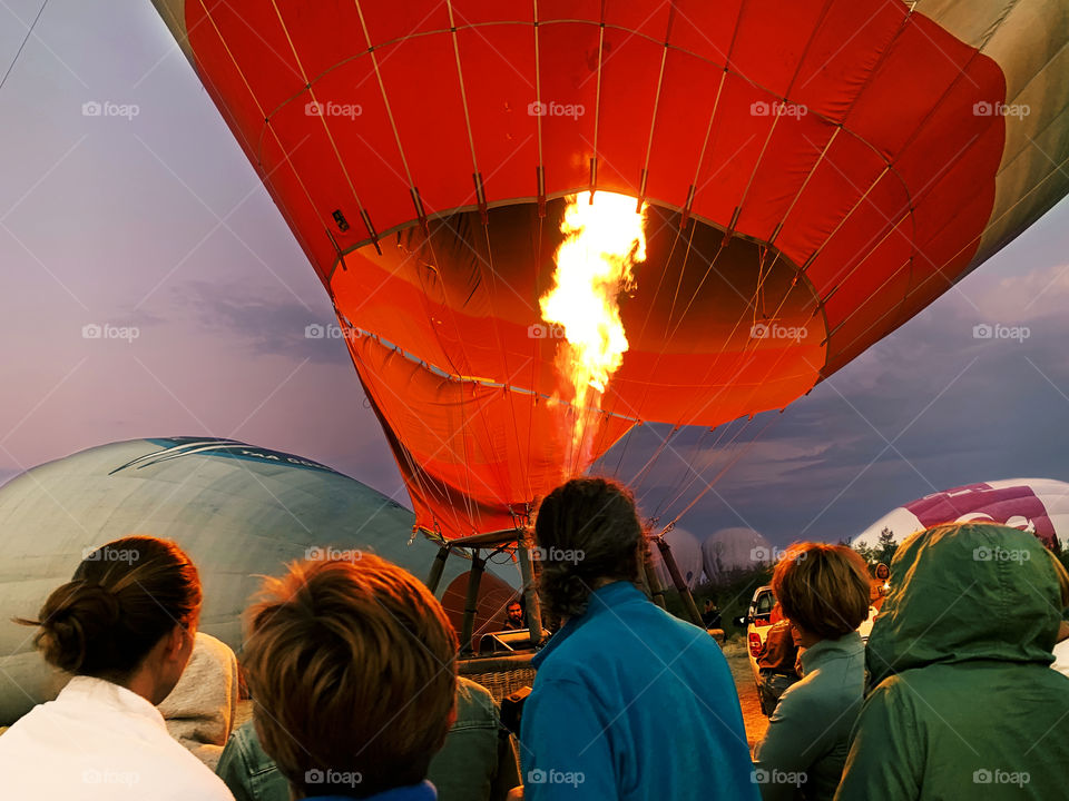 People watching the fire filling the red hot air ballon at sunrise 