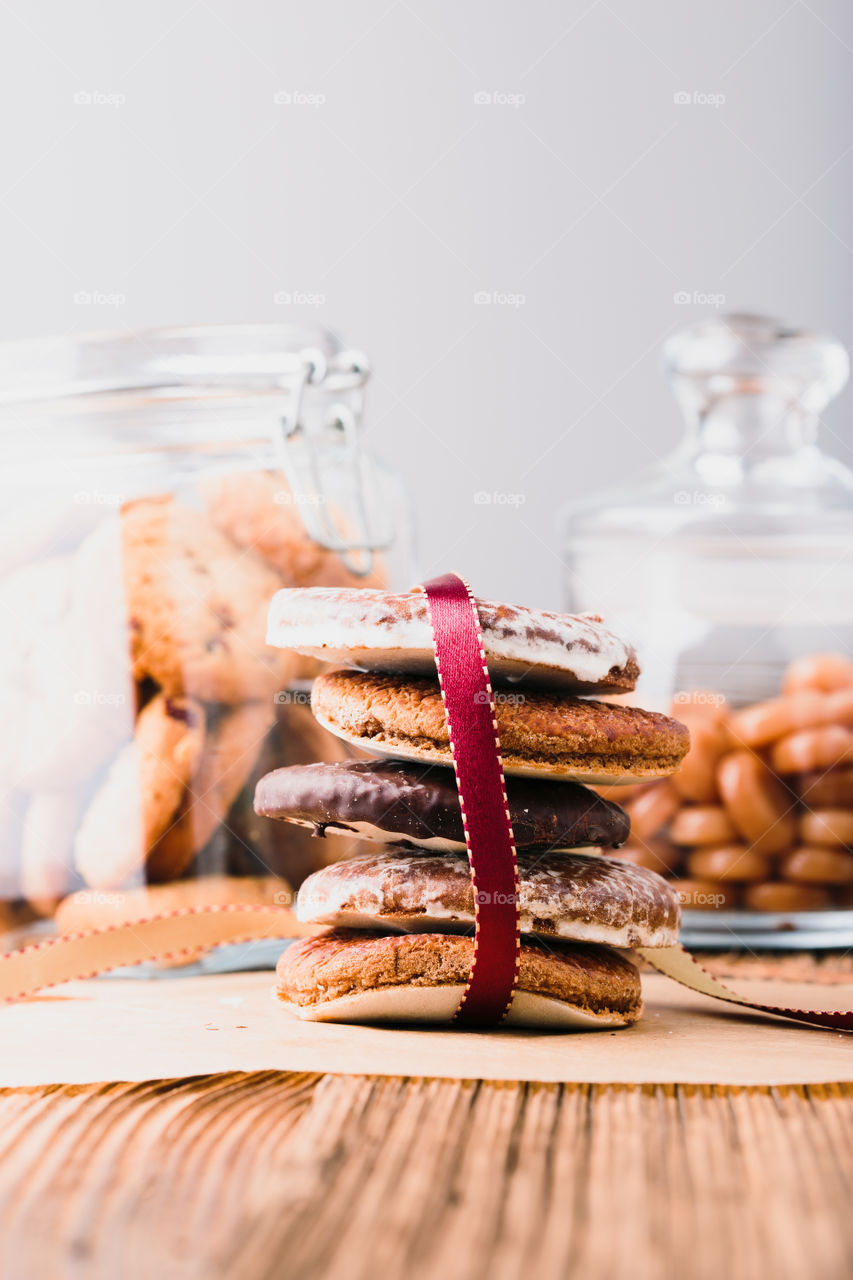 A few gingerbread cookies wrapped in red ribbon Happy Christmas on wooden table. Jars with sweets in the background