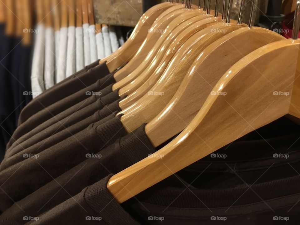 Brown and white T-Shirts hanging on wooden hangers on a retail rack display