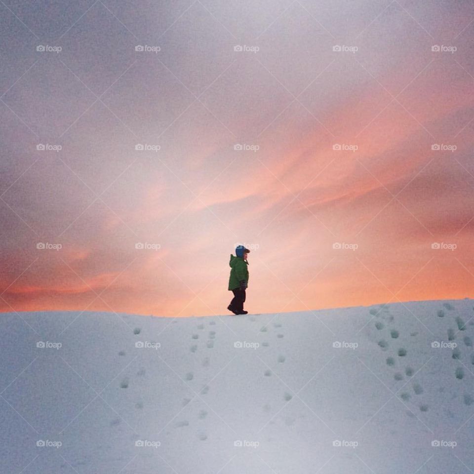 Boy on big pile of snow in sunset 