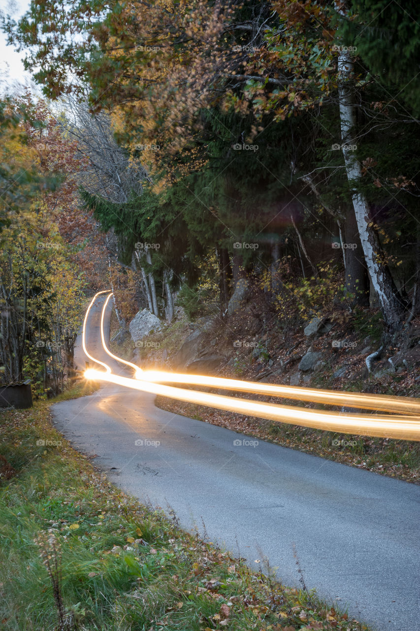 Light trails of a single car traveling along a winding country road surrounded by autumn foliage
