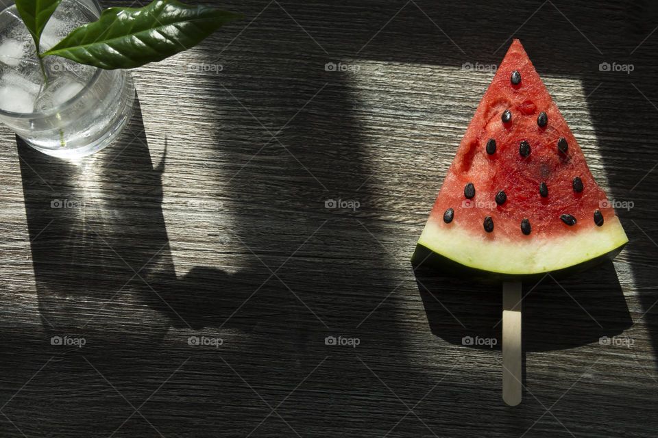 Portion of red watermelon with seeds in the form of a triangle on a wooden table surface