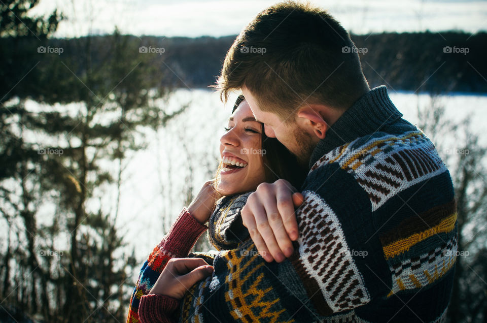 Joyful cute couple embraces. Young man in a sweater hugs a girl from behind background in winter.