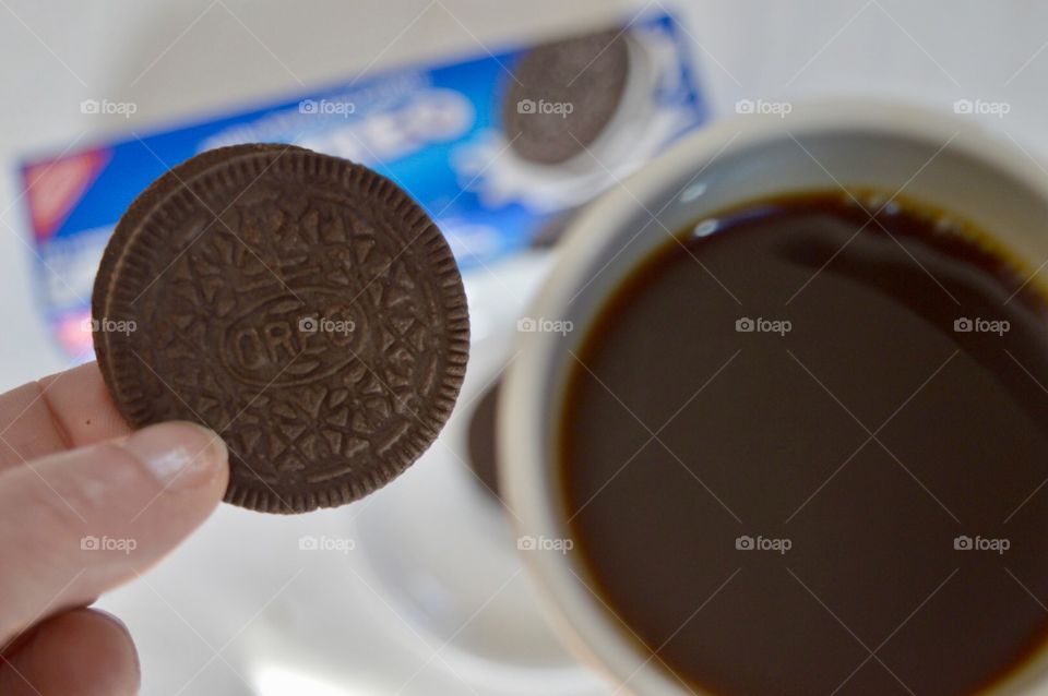Woman’s hand holding an Oreo cookie and a cup of coffee