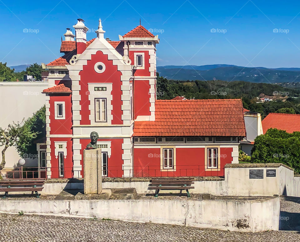 A large red, municipal building stands among green hills and under a late summer blue sky