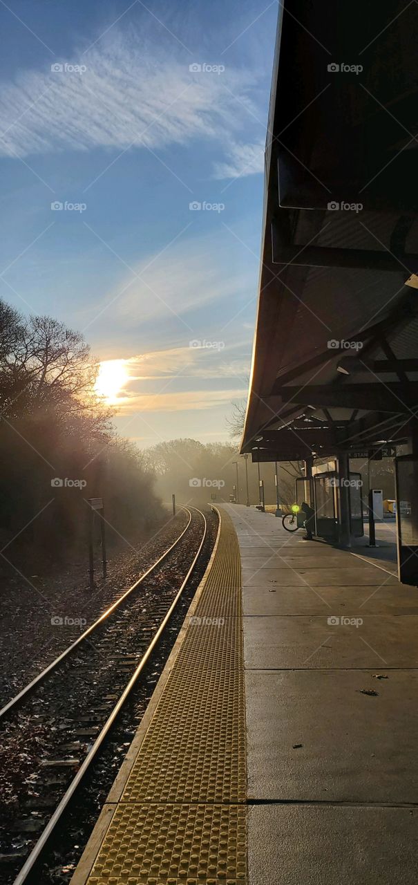 Early morning sunrise over train tracks showing through the hazy fog. Waiting platform empty before commuting into the city.