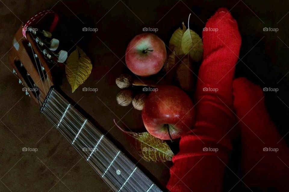 Autumn still life from above with a guitar, autumn leaves and nuts, red apples and legs in red knitted wool socks 