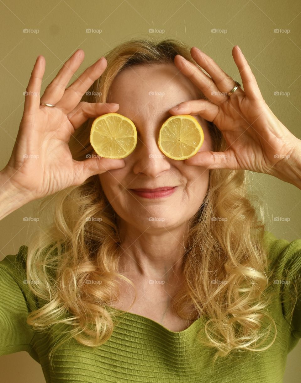 Look at those eyes, blonde woman wearing a green sweater, holding lemon slices over her eyes 