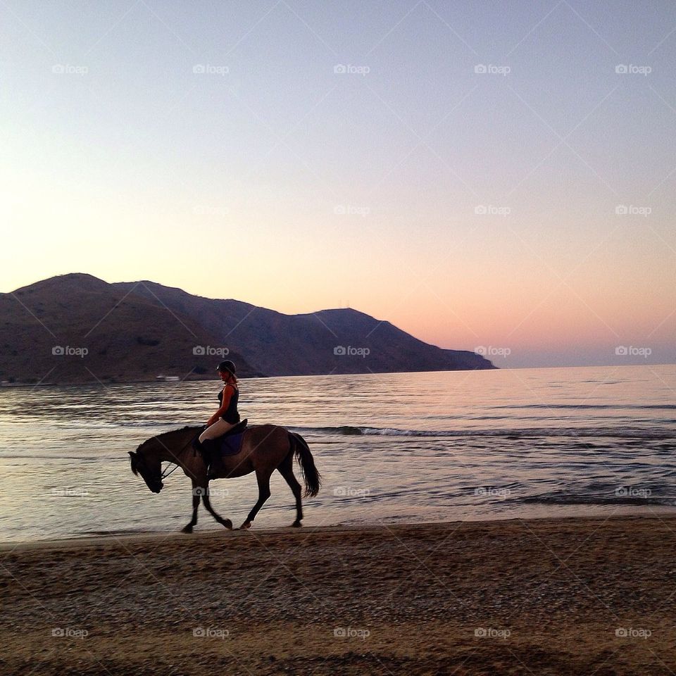 Person riding horse on beach at sunset