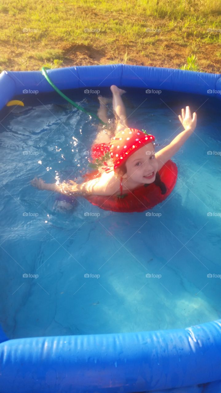 A beautiful 5-year-old, Molly, playing in her swimming pool on a red floatie- while rocking THE CUTEST little strawberry swim-set ever !!