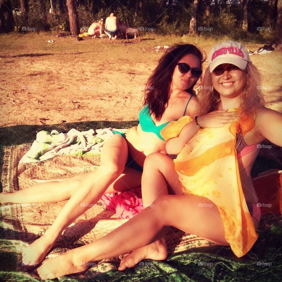 two beautiful girls Blonde and brunette sitting on the beach And smiling at the day