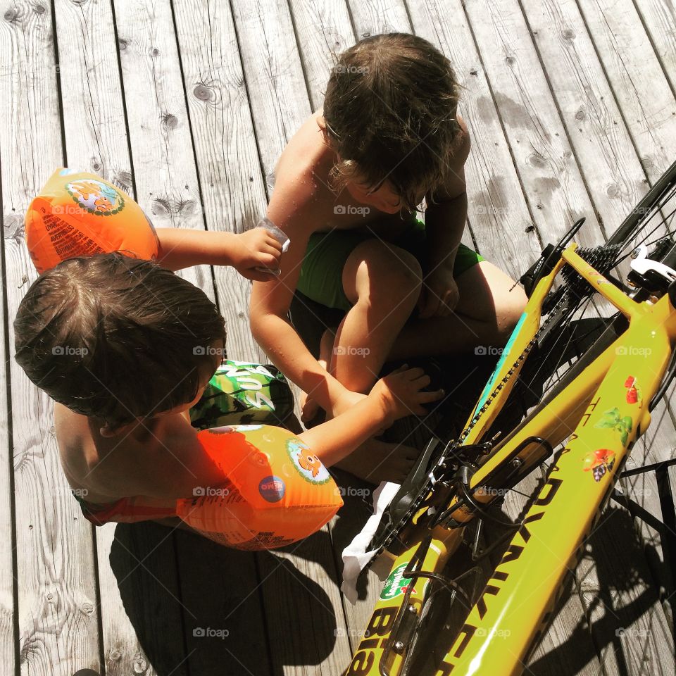 Two boys in swim pants clean yellow bike