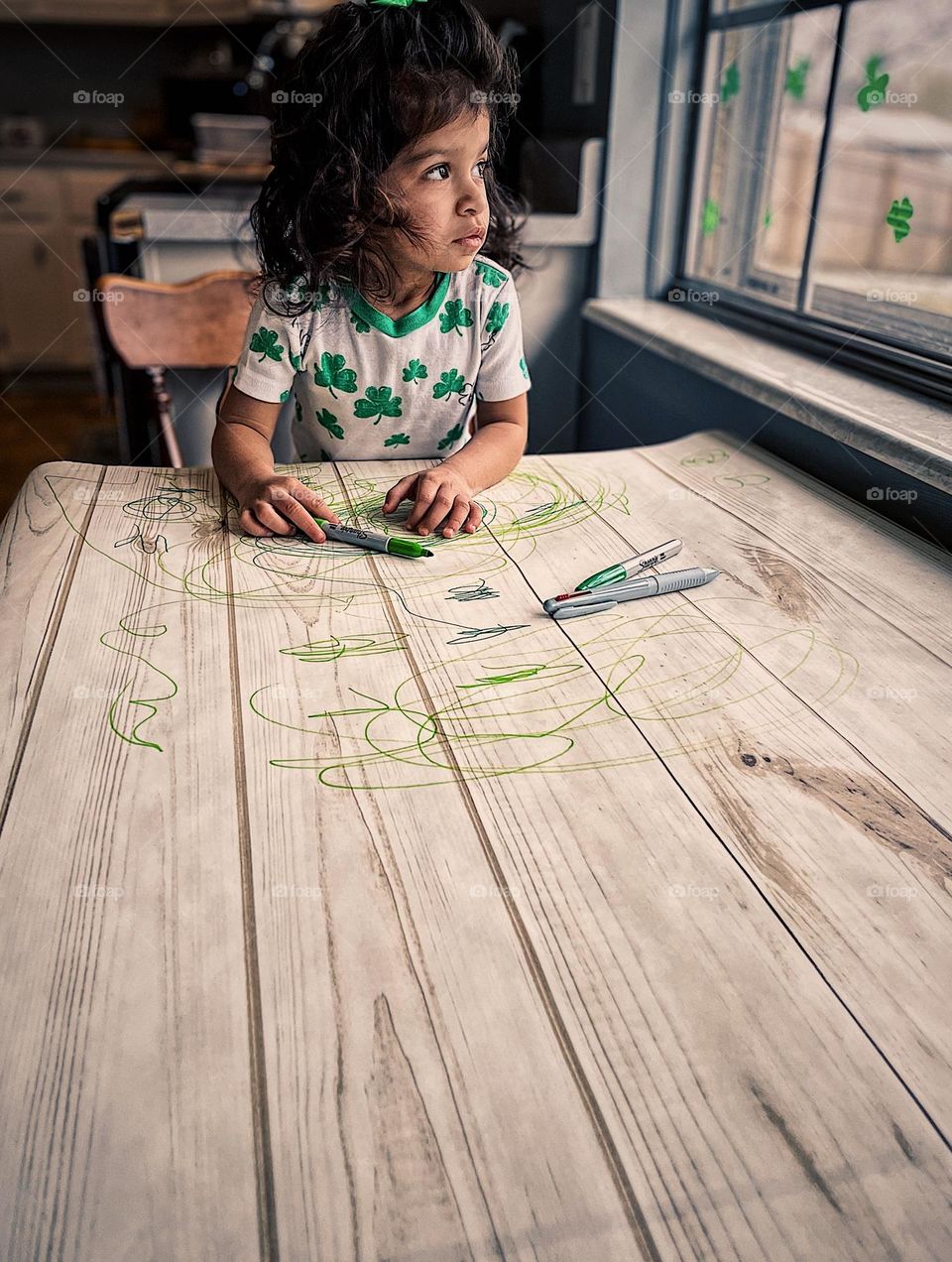 Toddler girl pondering while looking out window, toddler looking out window, little girl wishes she was outside, toddler girl making an art project by the window, toddler draws with Sharpie markers using natural light, portrait of a toddler 