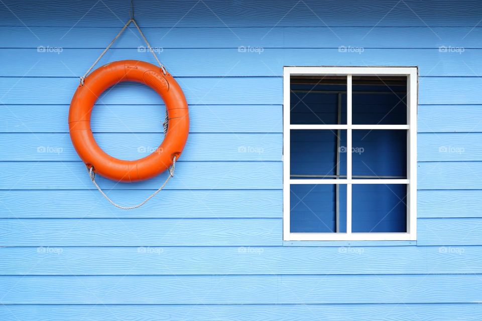 orange lifebuoy and white window frame on blue wooden wall 