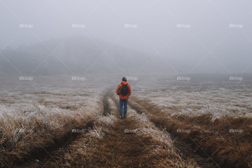 Photo of traveler man walking on field during foggy weather.