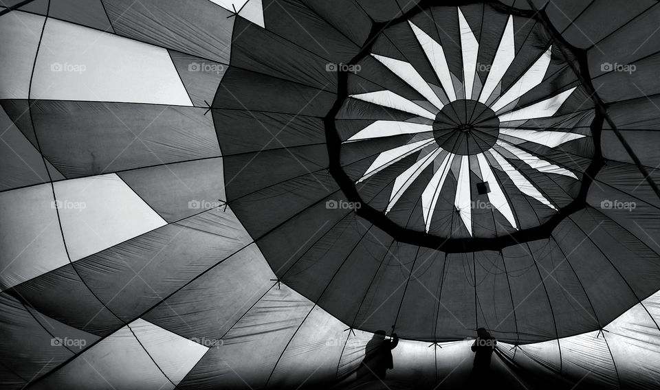 Inside a geometric design hot air balloon with silhouette of people on the outside helping assemble it.