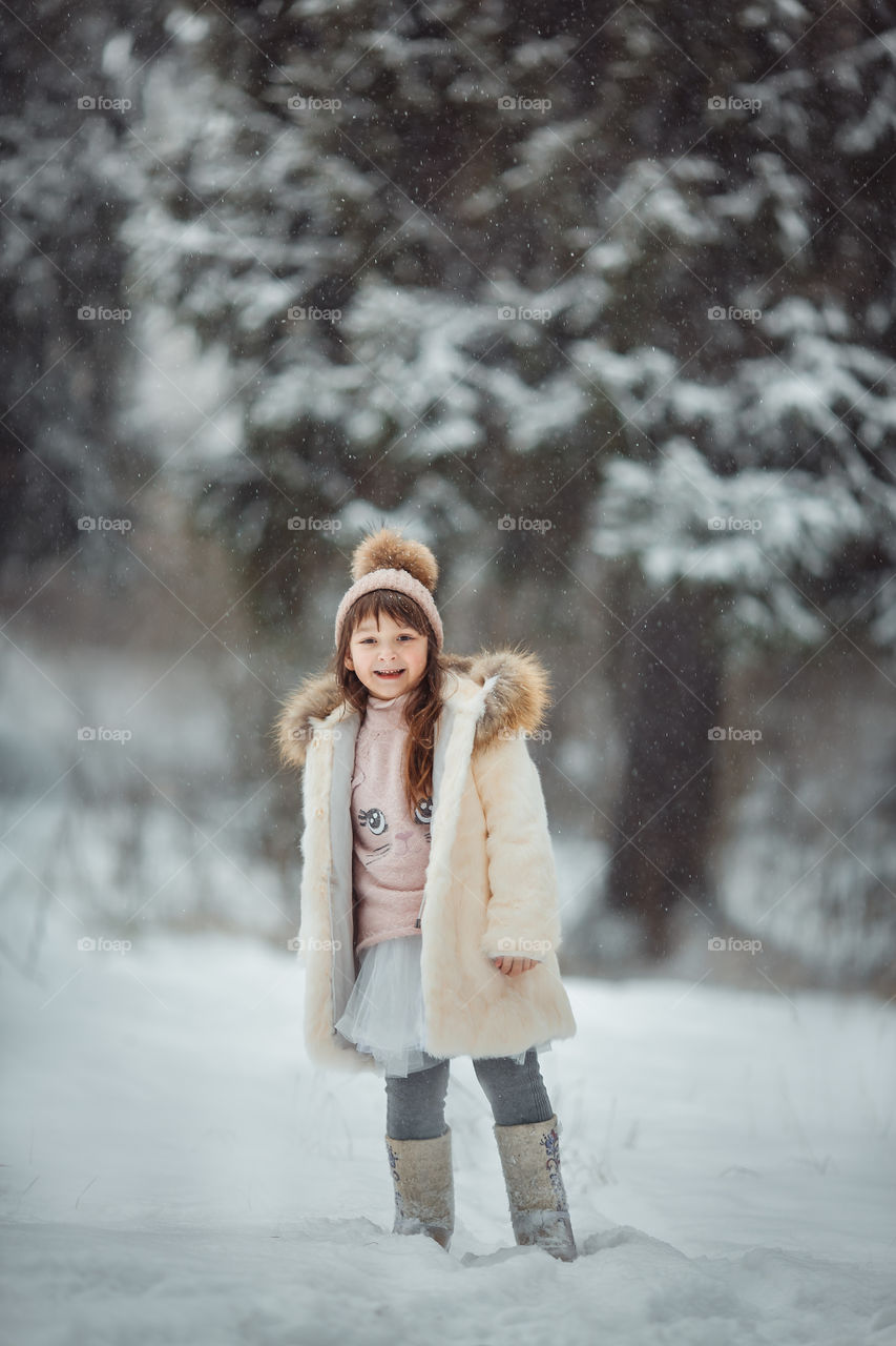 Winter forest at cloudy day. Little girl walking