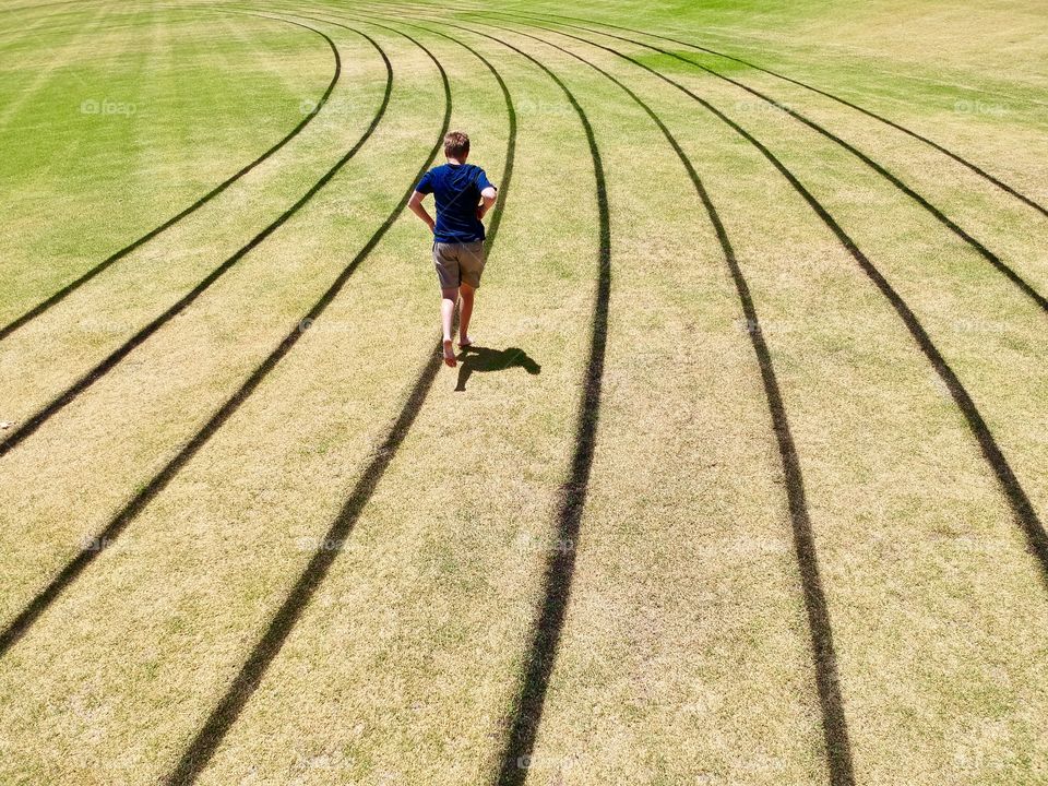 Boy jogging in bare feet around an oval marked with lane lines
