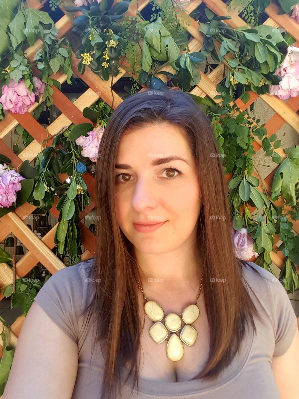 Front view of woman with necklace against leaves and fence