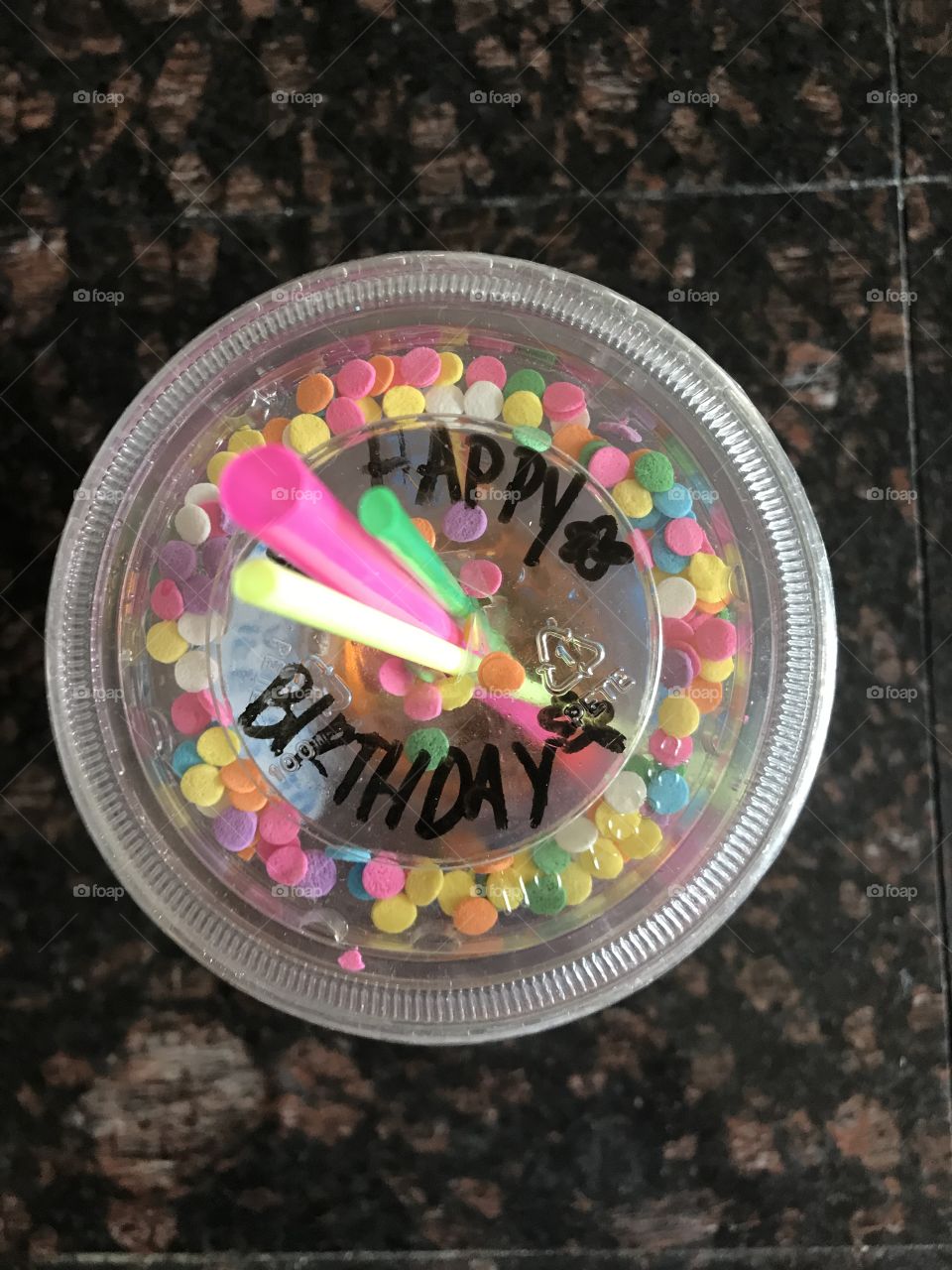 Happy birthday writ time on cup with rainbow colored candy sprinkles 