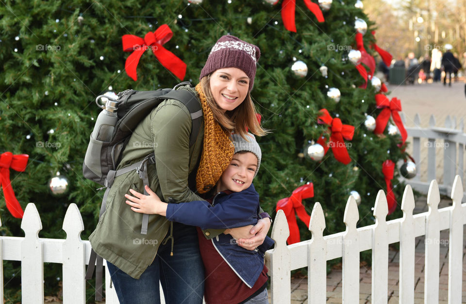 Mother and son hugging in front of a Christmas tree outdoors