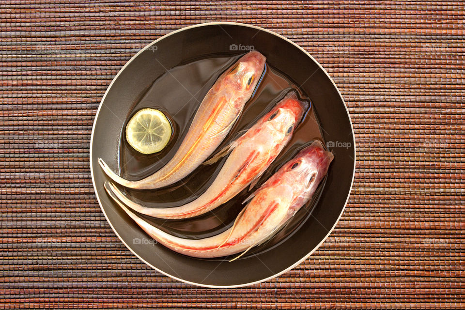 The fresh fish is cleaned and prepared for cooking with lemon and spices in oil in a pan on a natural Mat background. Recently caught gurnard. Food photos