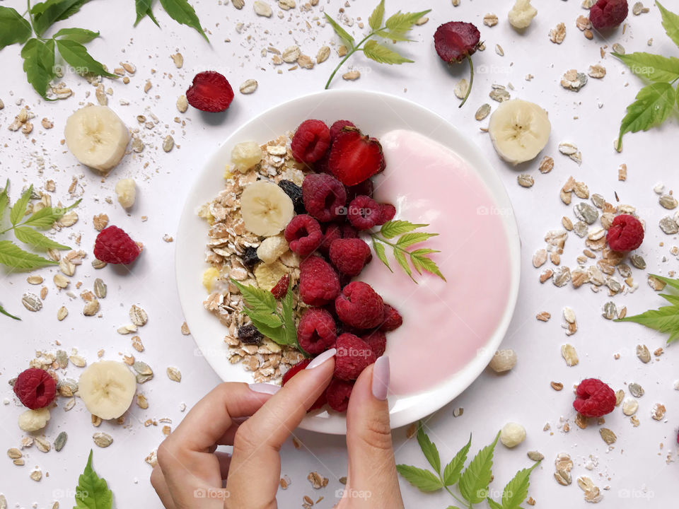 Female hand taking a red red raspberry out of the plate with yogurt, berries and muesli 