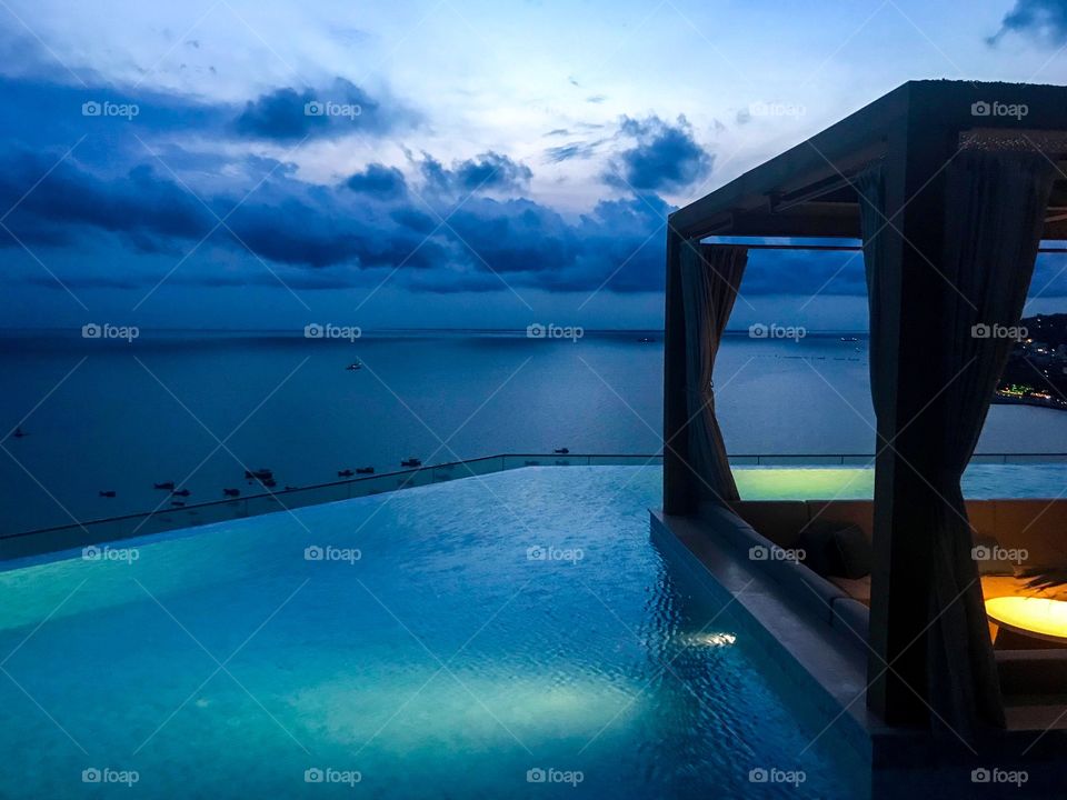 swimming pool with blue water,the corner was a place to sit with a table, a roof and a curtain,in the sky there are dark blue clouds, dark blue sea water, blue background