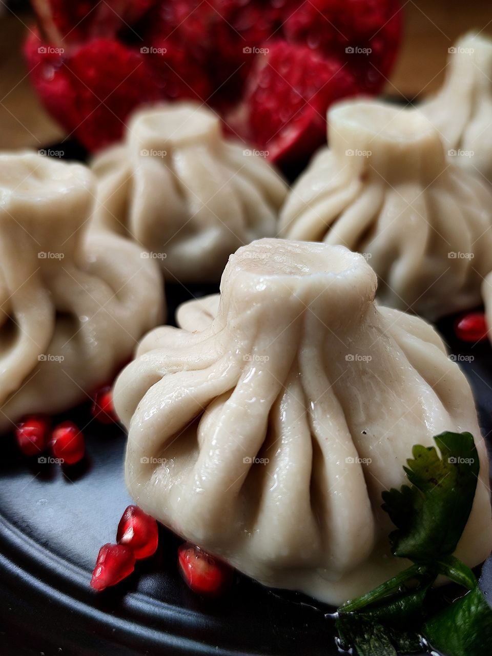 Food.  On a black plate are khinkali, red pomegranate seeds.  Chopped pomegranate in the background