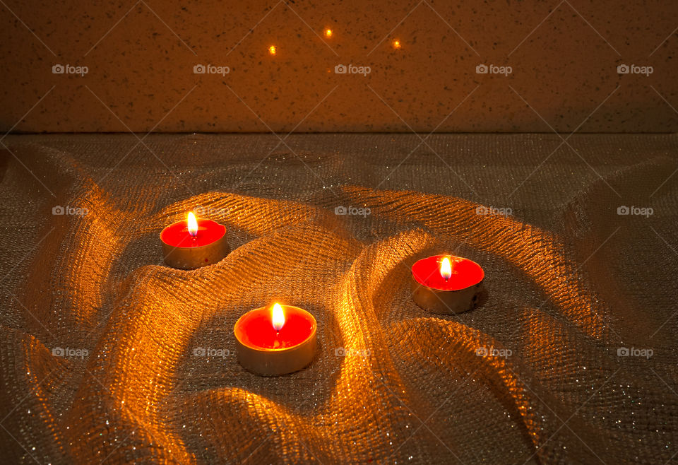 Close up view of three romantic candles are standing on the shiny fabric in the dark