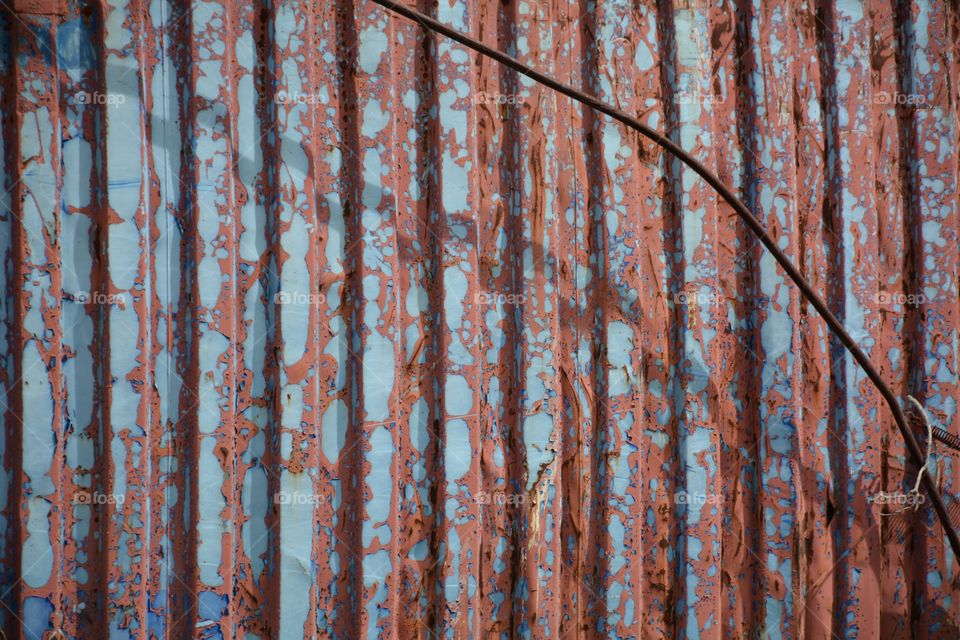 Blue and red peeling paint on corrugated metal siding