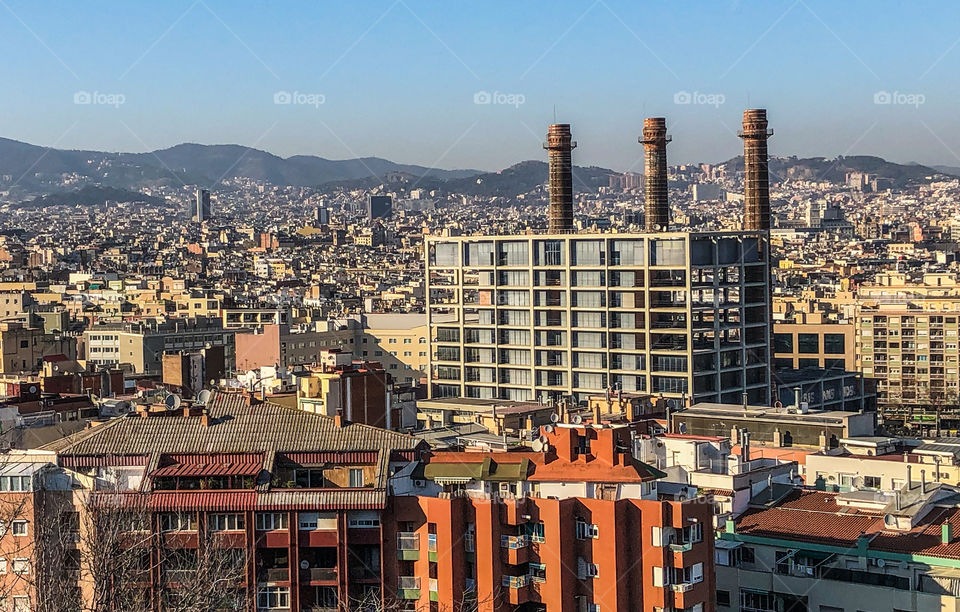 A view of the city from Montjuïc, Barcelona. Mostly urban dwellings and industrial buildings with distant mountains along the skyline