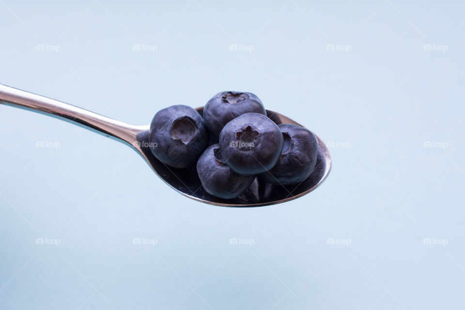 A spoon filled with blueberries, light blue background 
