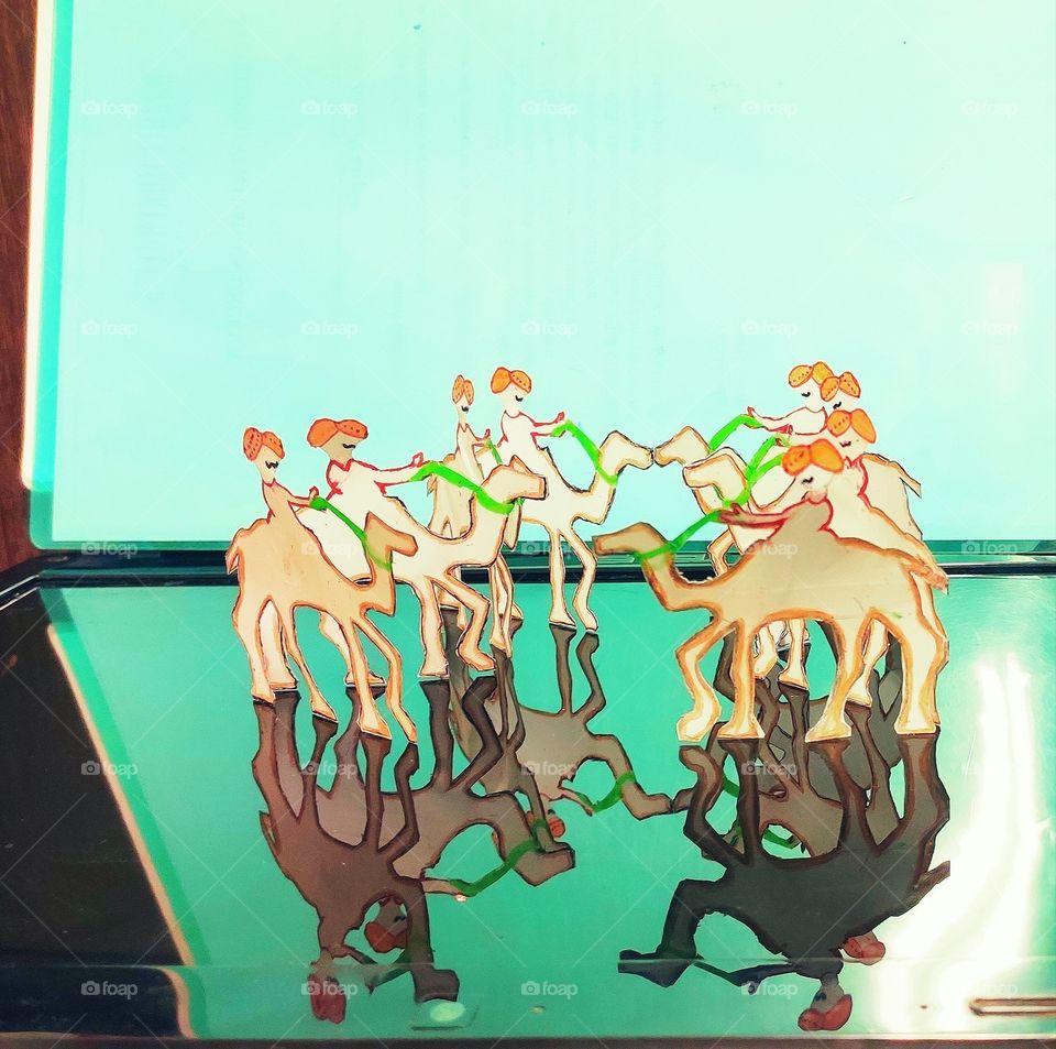 Seeing double via mirror effect, creative paper cutting decoration in office on Rajasthan's Day- 30th March. Camels and their owners assembly is being held before camel race. Lights effect seen in reflection as some camels appear brown or acutal one.