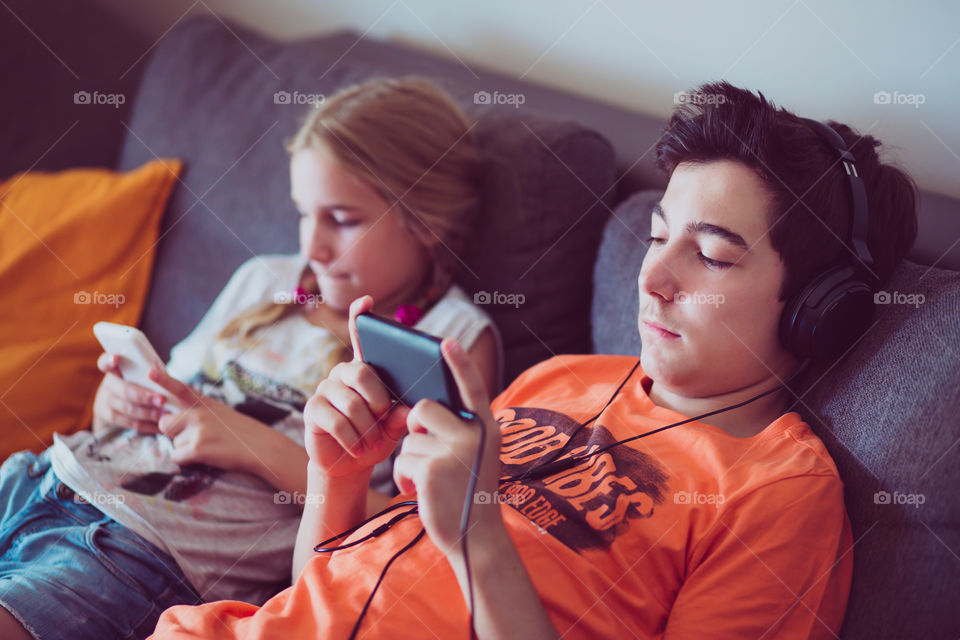 Brother and sister sitting using mobile phone on sofa