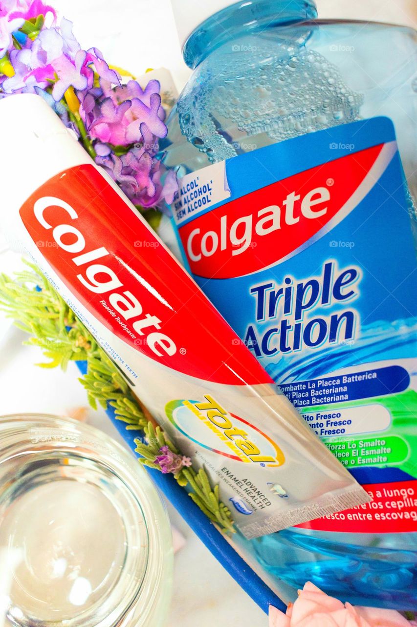 Close view of Colgate toothpaste and mouthwash. Surrounded by a glass with some mouthwash and flowers
