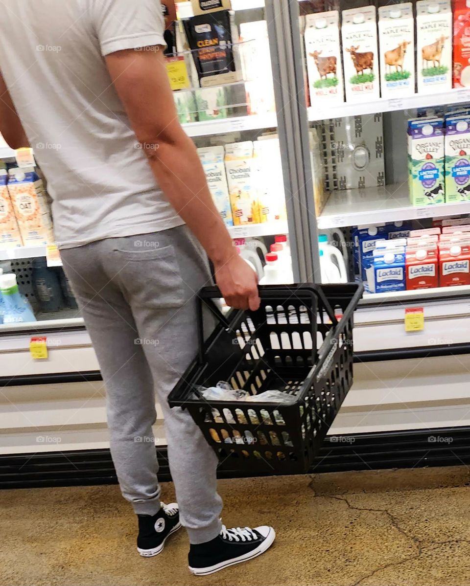 view of a man wearing black sneakers with a basket shopping in the dairy section of an Oregon market