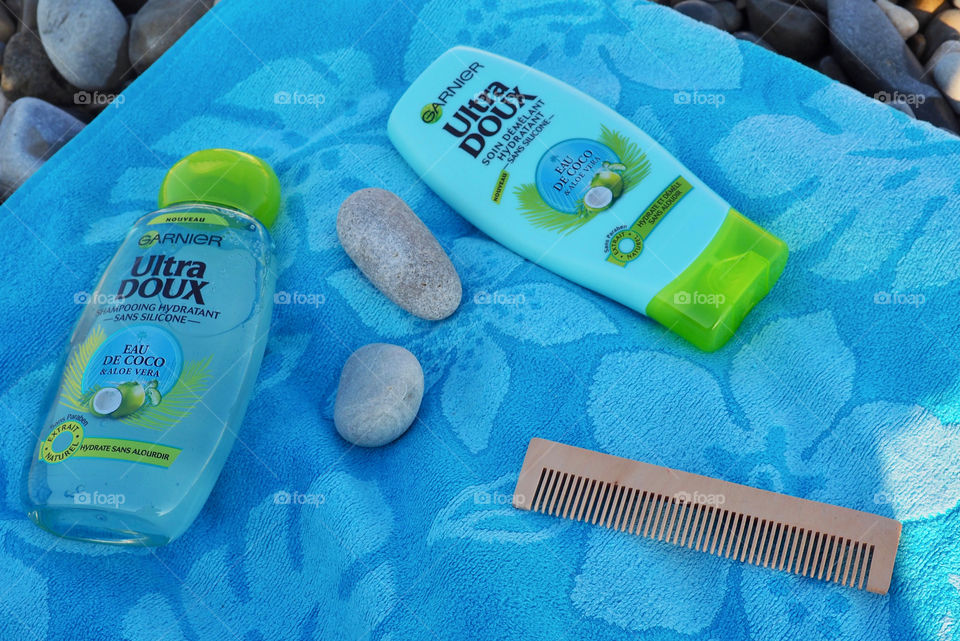 Garnier eau de coco shampoo and conditioner on a blue beach towel with comb and beach stones.