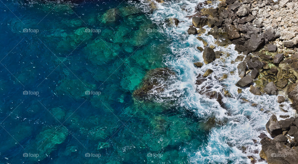Blue ocean crashing on rocky coast seen from above 