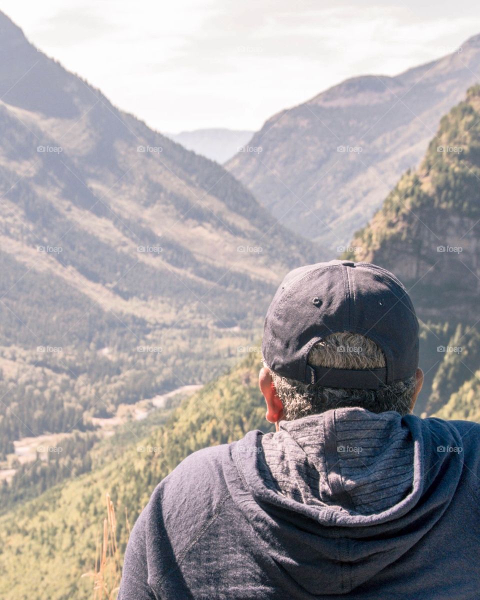Man in baseball cap and hoodie in foreground looking out at the mountains 

