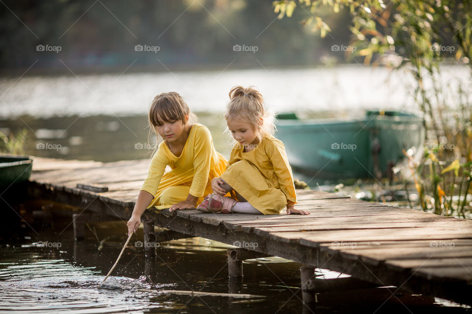 Little sisters playing near lake at autumn day 