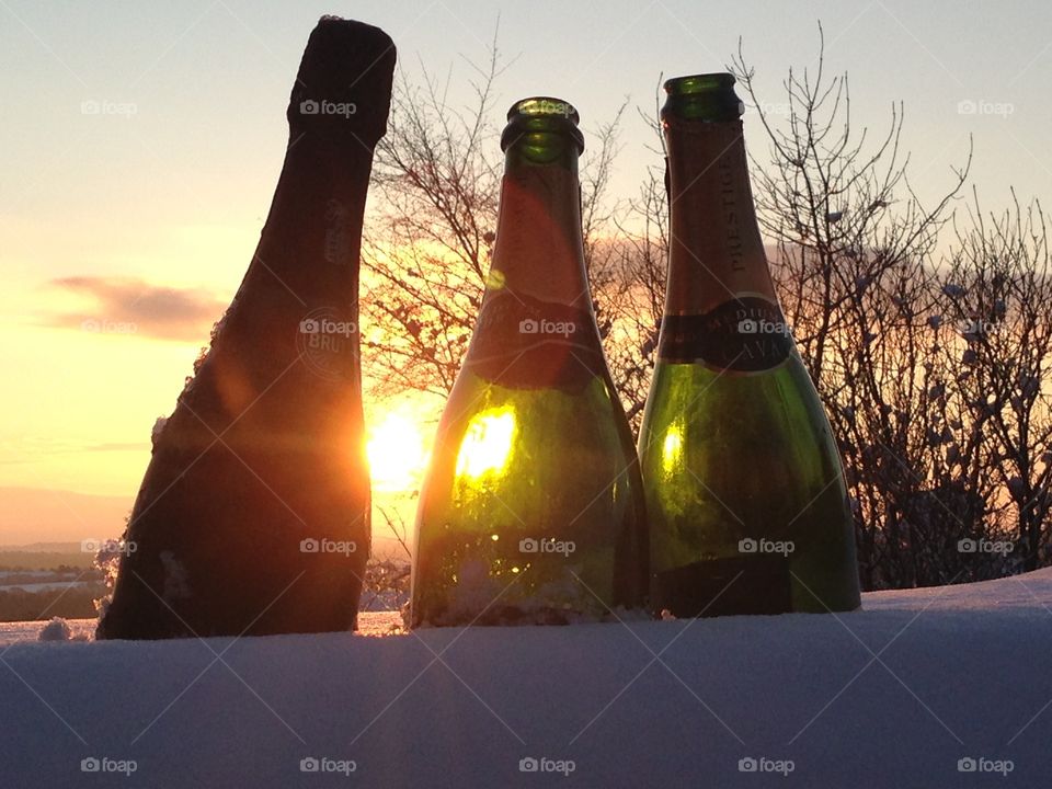 Champaign bottles in snow with the sun behind 