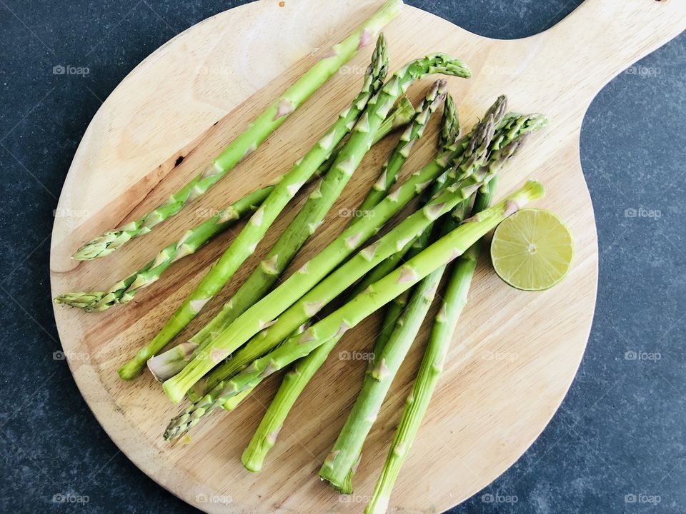 Wooden plate with healthy green asparagus, accompagnied by half a green lime. Plate design, food art.