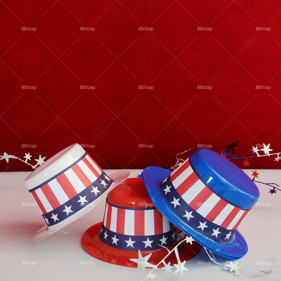 Tiny party hats in red, white, and blue with the Stars and Stripes for hat bands on a table with confetti. 