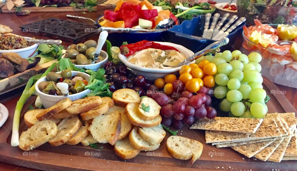 Table set with hors d’oeuvres at a social gathering including, crackers, bread, hummus, fruit and olives