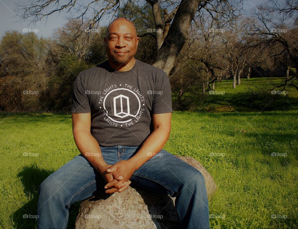 a man sitting on a rock with a smile on his face enjoying a beautiful day in nature