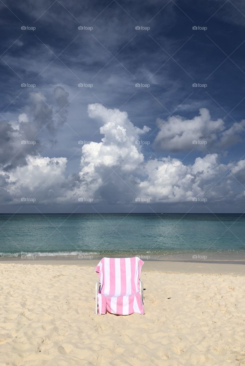 Pink and white striped towel on beach chair with the ocean and sky in the background 