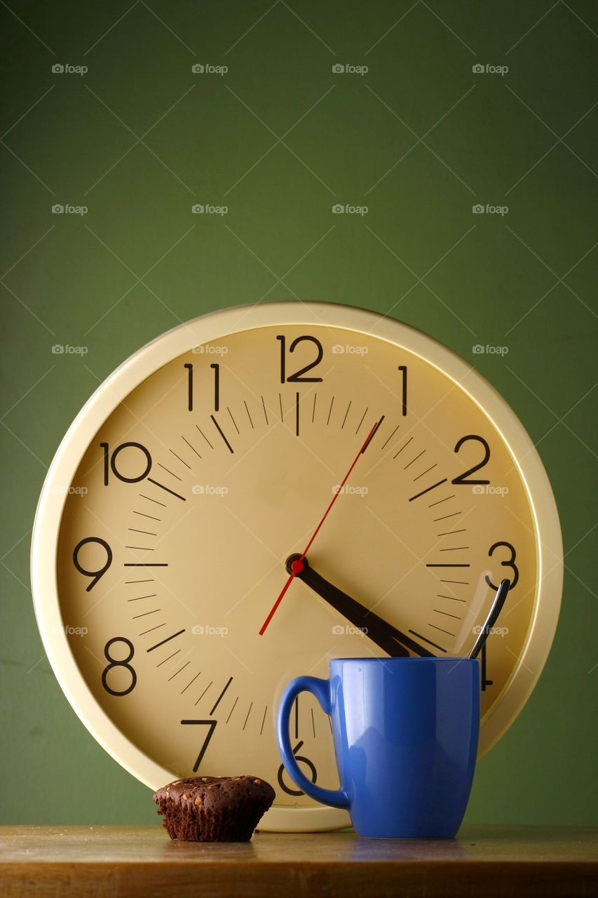 blue coffee mug with teaspoon, a brownie and an analog clock